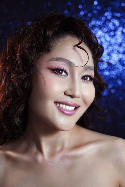 Free Portrait of a smiling woman with curly hair against a sparkling blue background. Stock Photo