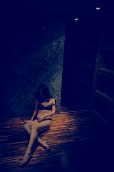 Artistic portrait of a woman in lingerie seated on wooden floor under dim lighting.