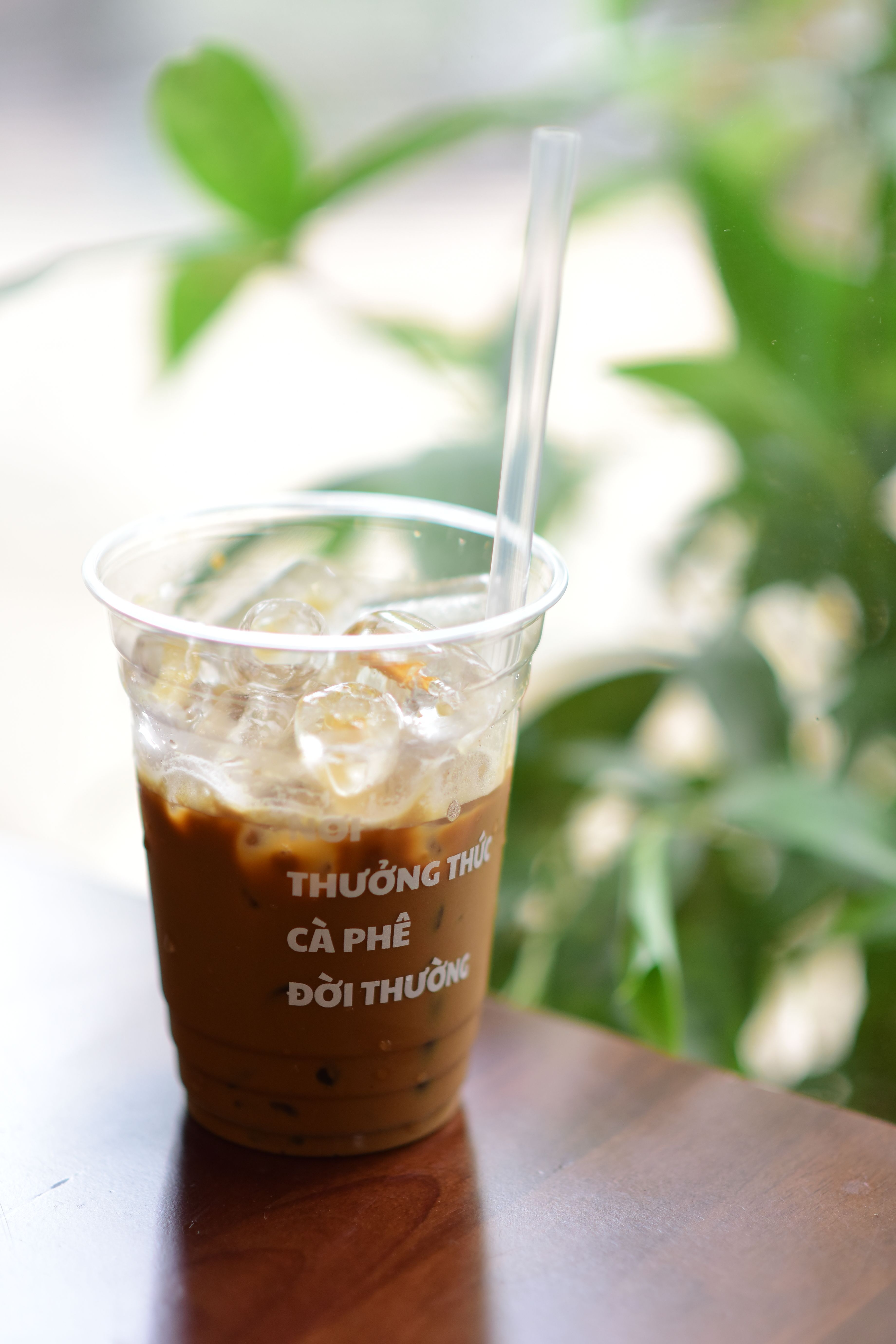 Delicious Vietnamese iced coffee in a clear cup with ice cubes, set in a lush green environment.
