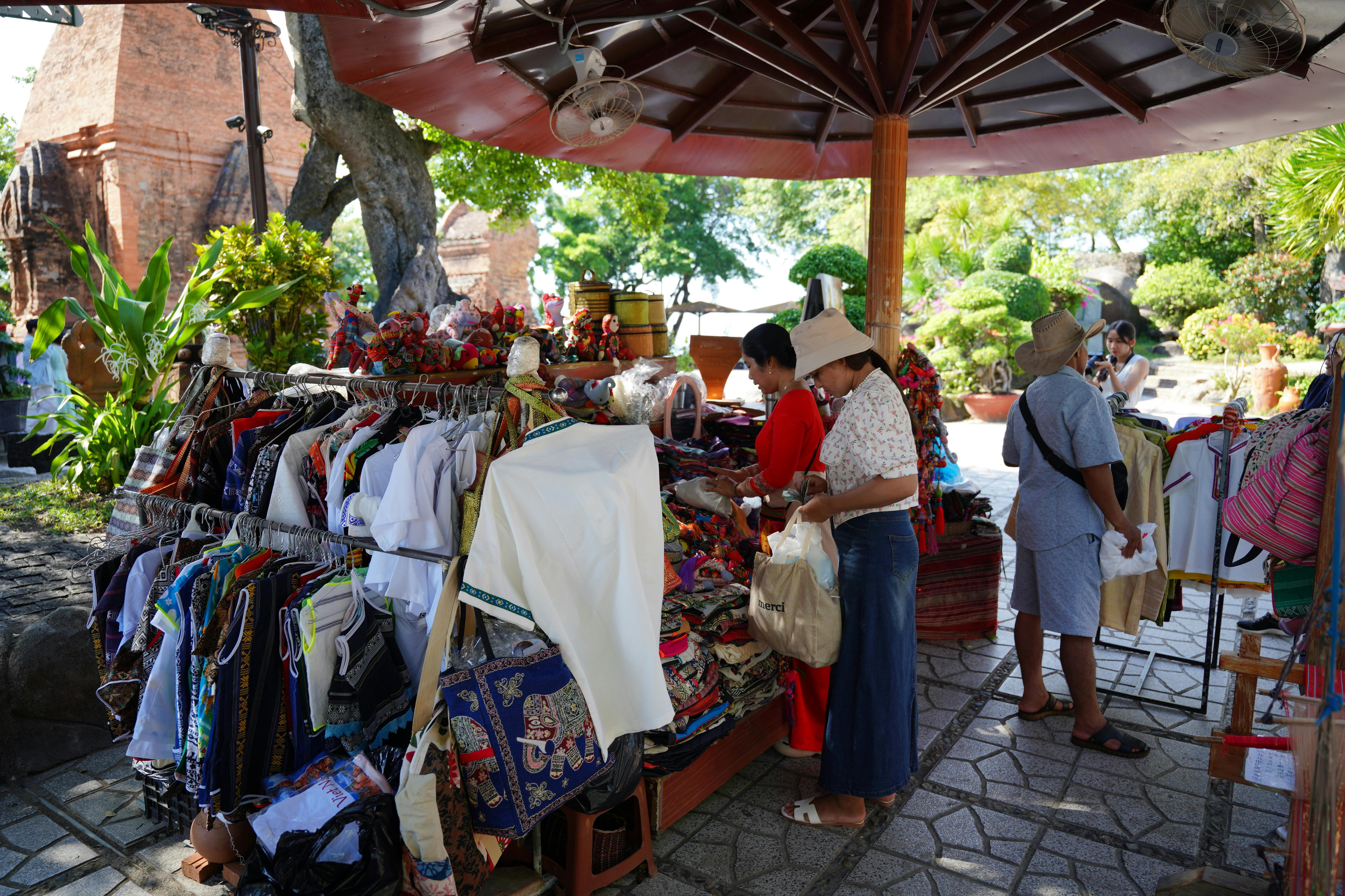 People shopping at a vibrant outdoor market stall with colorful clothing and crafts in Asia.