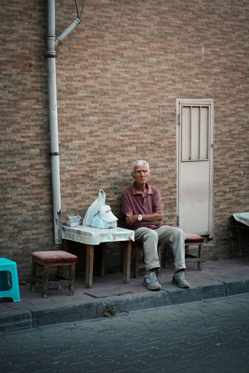 Free Senior man sitting alone on a street bench against a brick wall, looking thoughtful. Stock Photo
