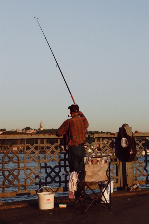 Free A man fishes on a bridge during sunset, casting his line into the water. Stock Photo