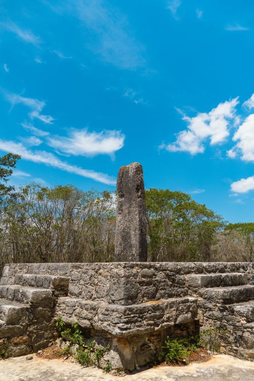 Free Stone monument in Dzibilchaltún, showcasing ancient Maya architecture under a vibrant blue sky. Stock Photo