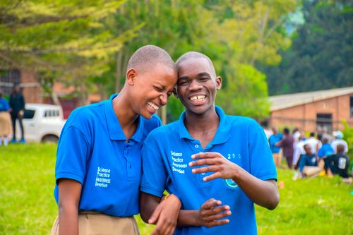 Free Two students in blue uniforms sharing a joyous laugh in a schoolyard setting. Stock Photo