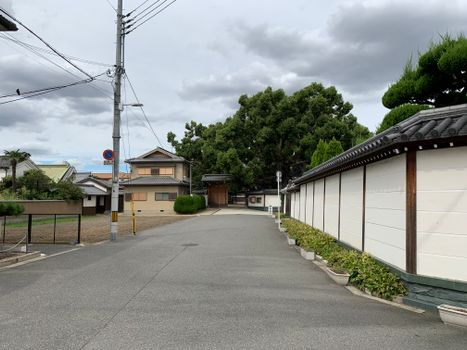 A peaceful Japanese street with traditional homes and lush greenery, illustrating serene urban life.