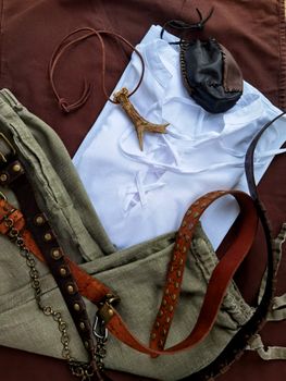 Flat lay of medieval-inspired clothing and accessories on a brown background.