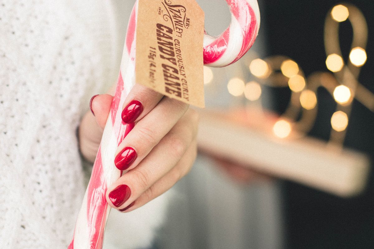 A festive candy cane held by a hand with red polished nails, perfect for Christmas decor.