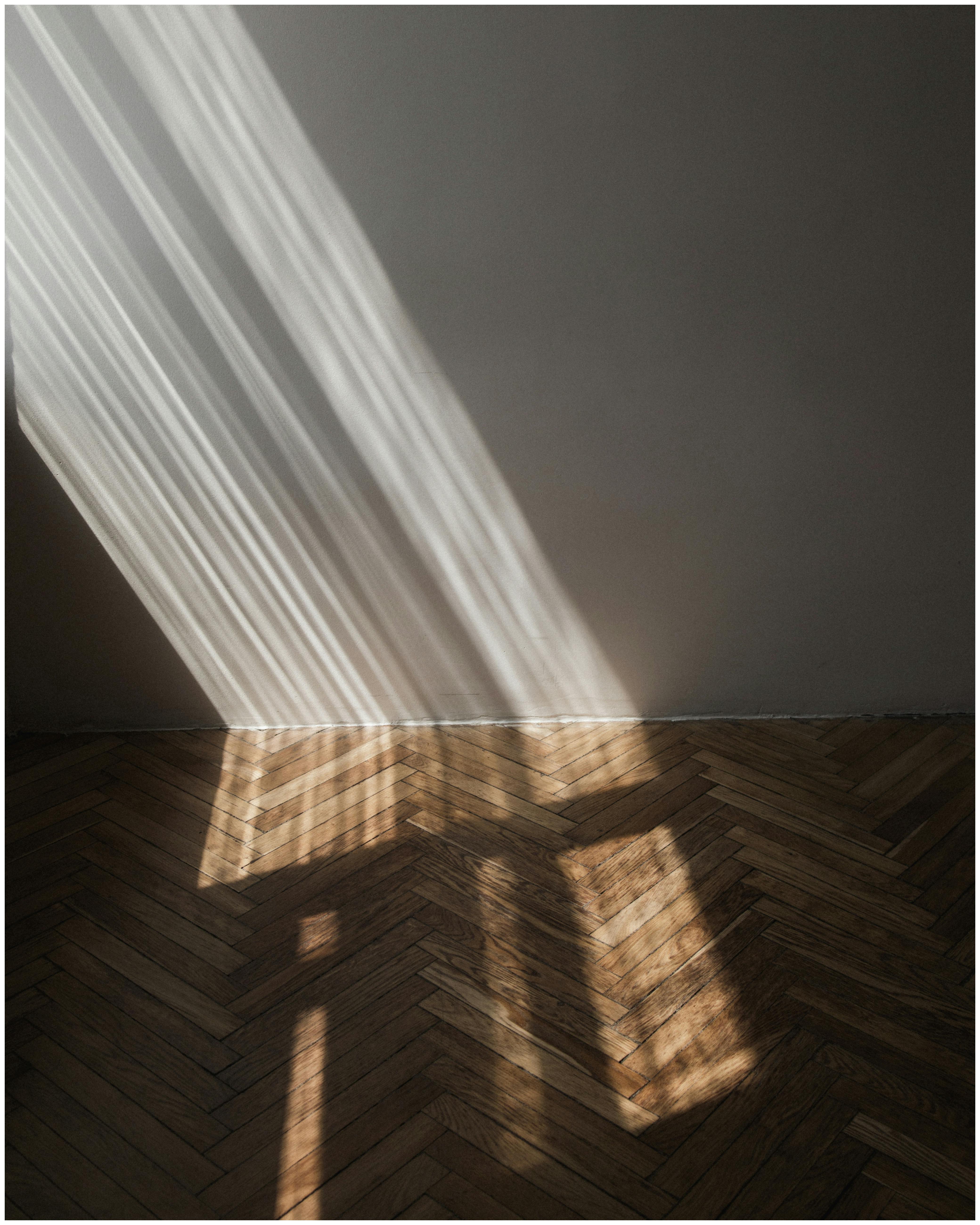 Sunlight casts dramatic shadows on a wooden floor creating a serene minimalist scene.