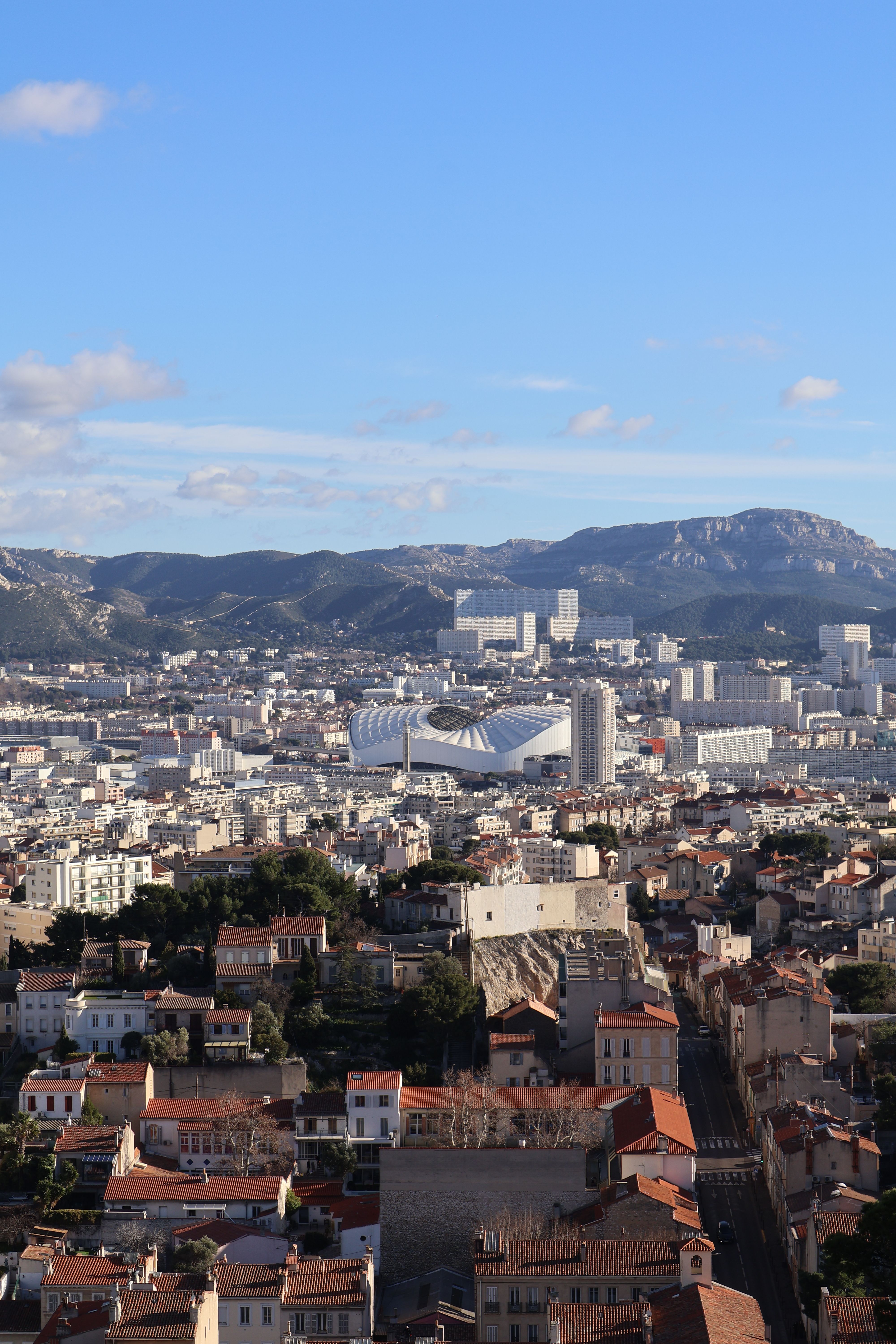 Scenic aerial view of Marseille, France, showcasing urban architecture and distant mountain ranges under a clear blue sky.