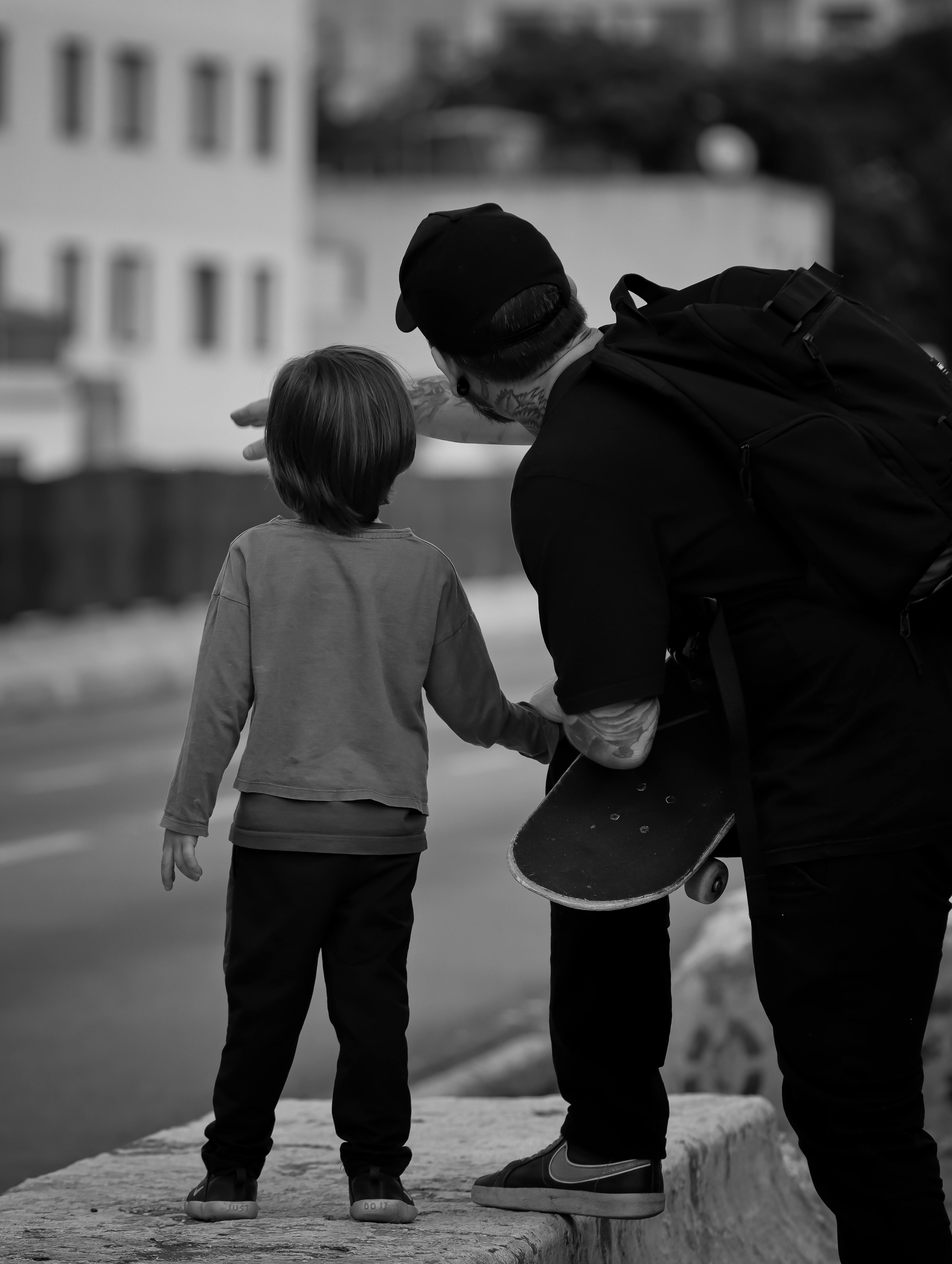 A father and son share a moment on a city street, holding a skateboard, enjoying quality time together.