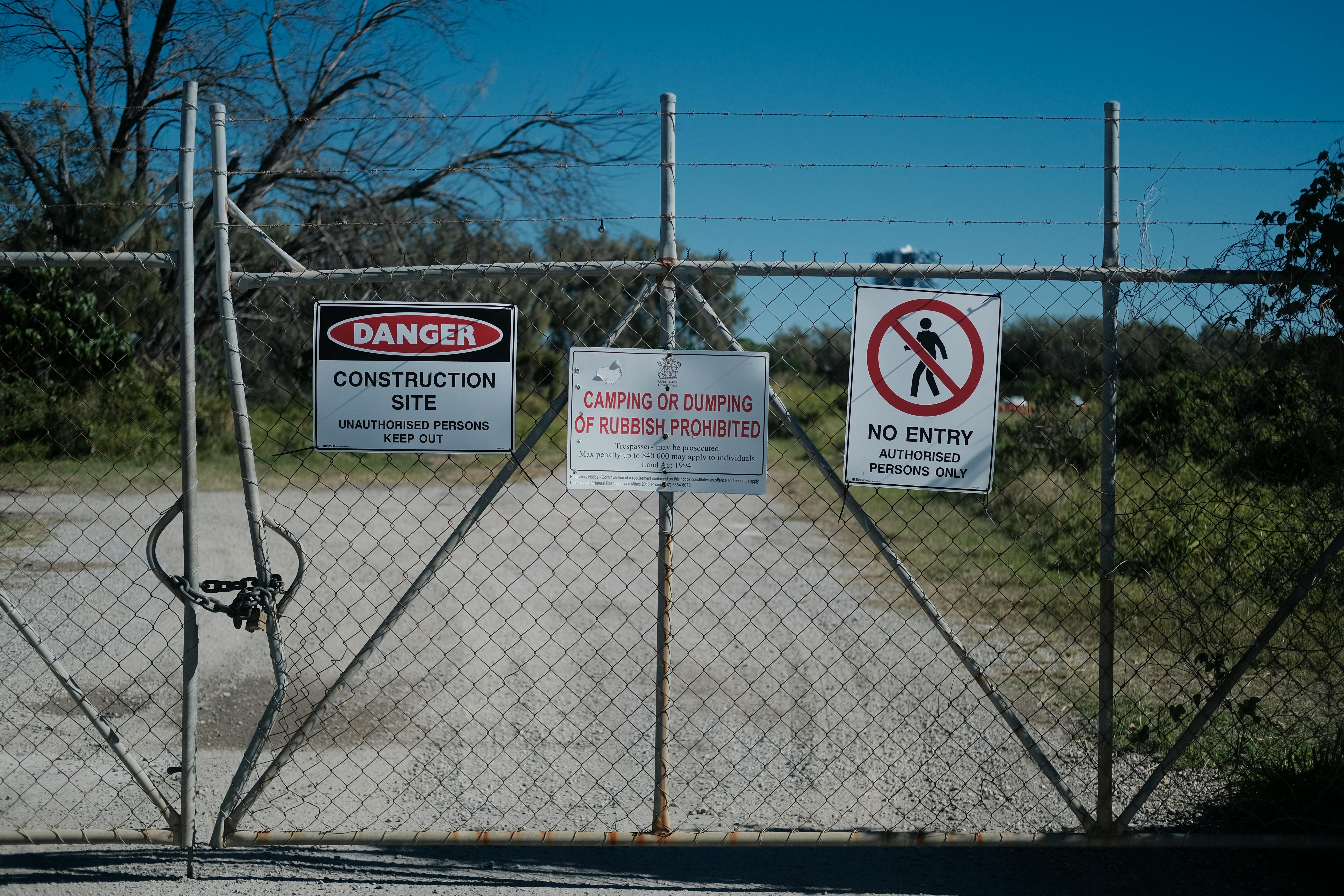 Metal gate with warning signs at a construction site prohibiting entry and dumping.