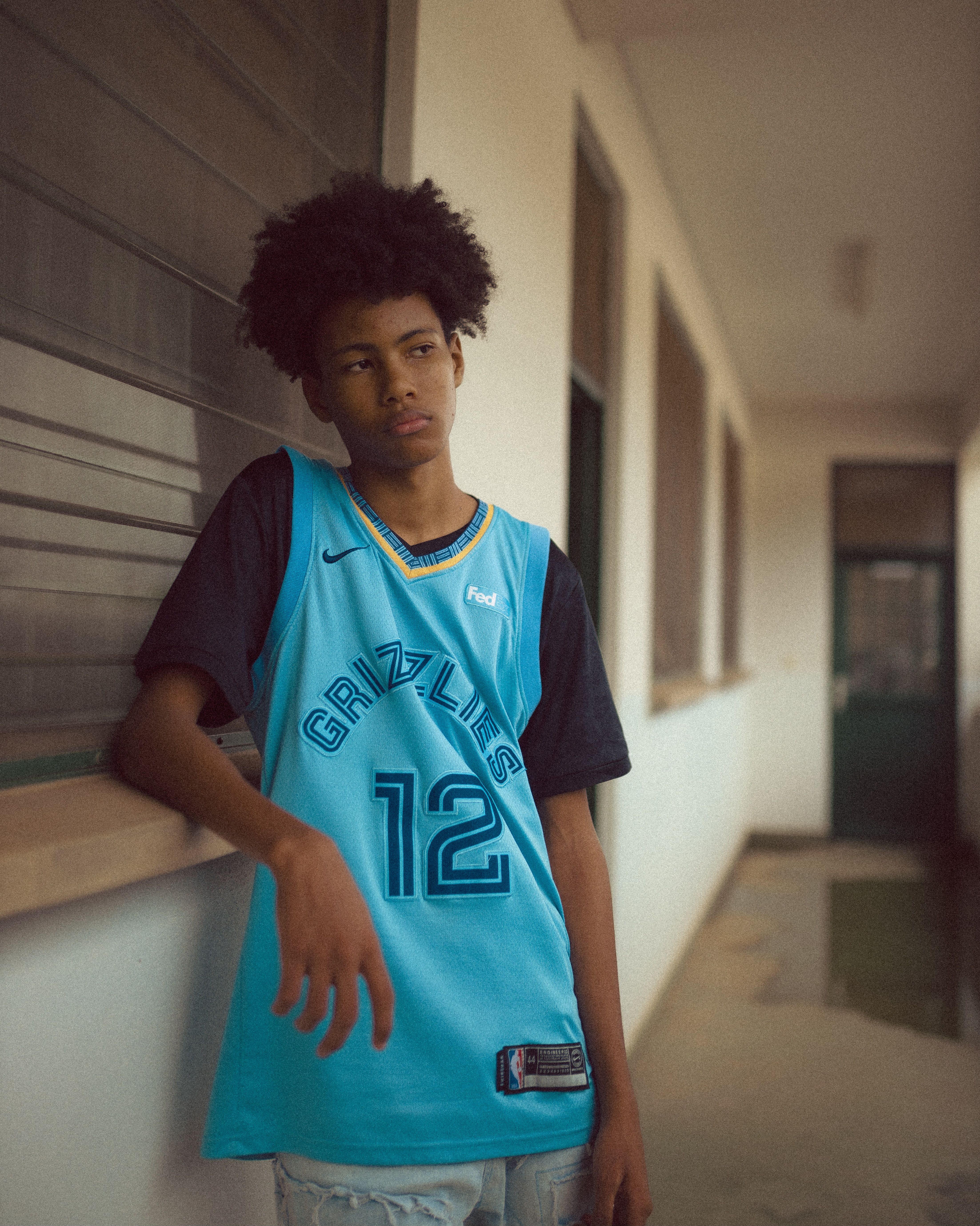 Teenage boy in sports jersey leans casually against a wall. Bright and contemplative mood.