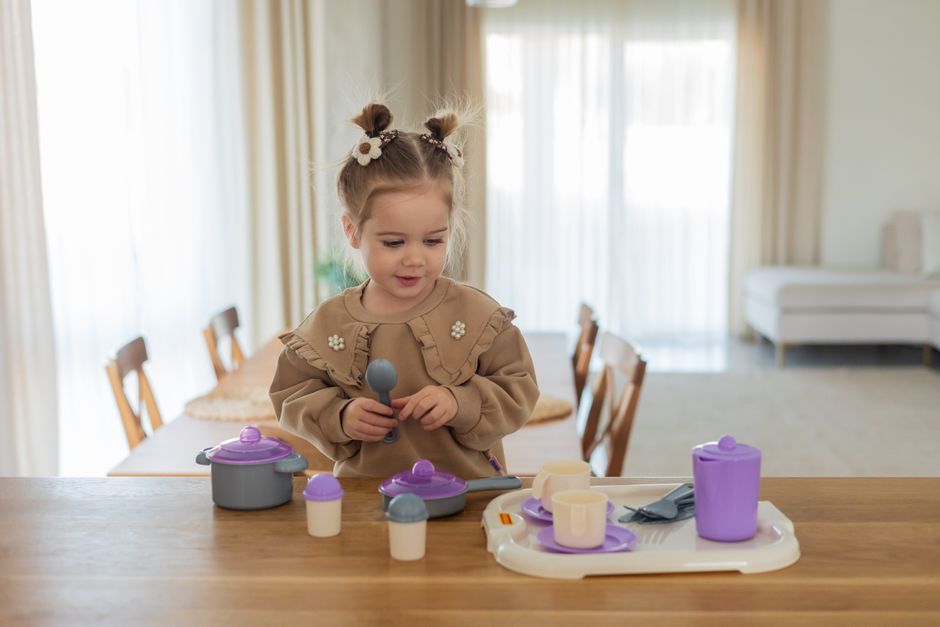 Little girl enjoying imaginative play with toy kitchen set in a cozy, well-lit room.