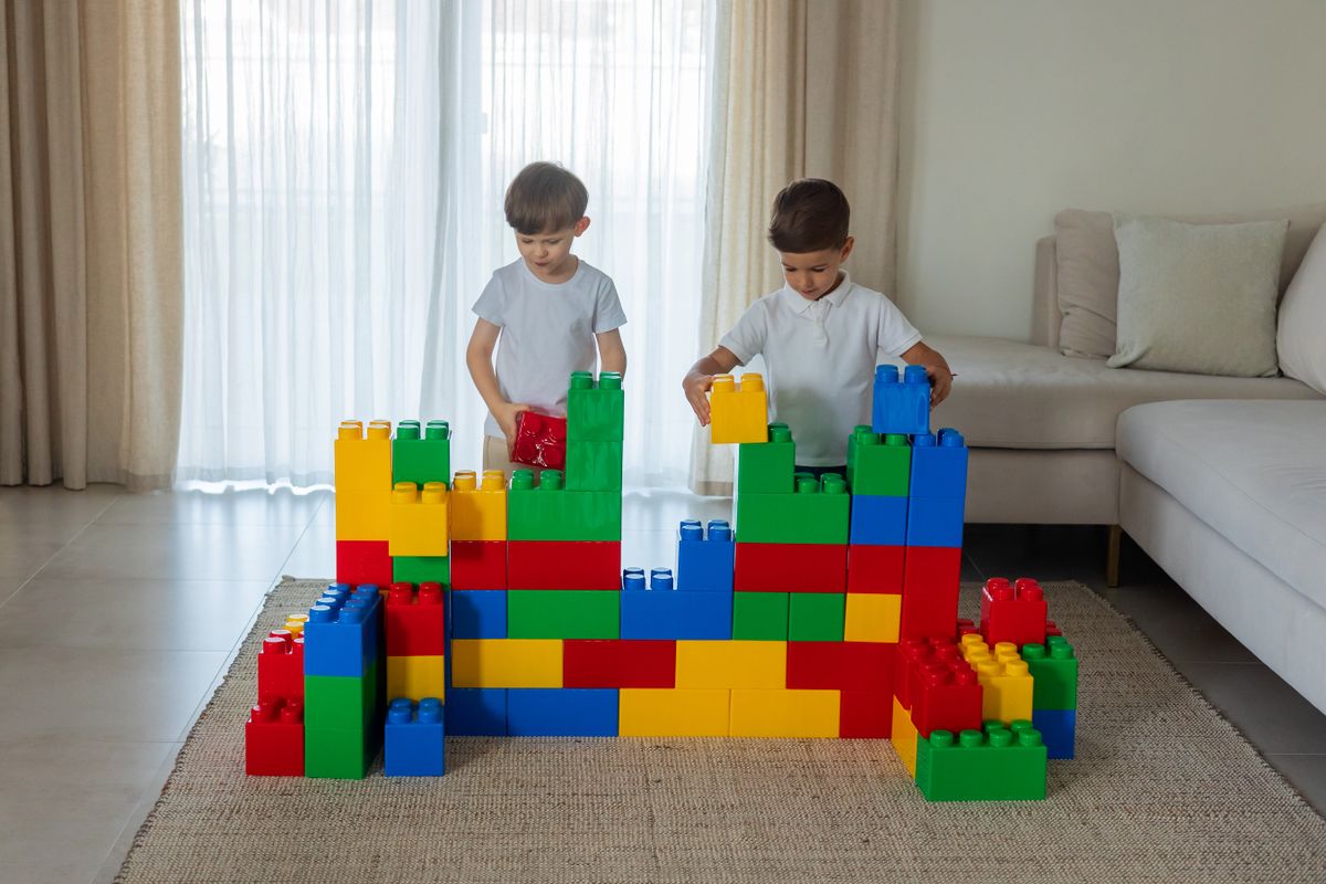 Two young boys building a large wall from colourful bricks