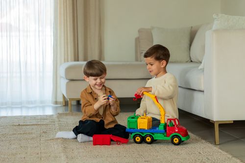 Free Two young boys enjoying playtime with a colorful toy truck in a modern indoor setting. Stock Photo