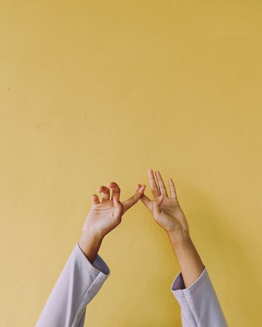 Two hands gracefully reach up against a bright yellow wall, creating a minimalist and artistic composition.