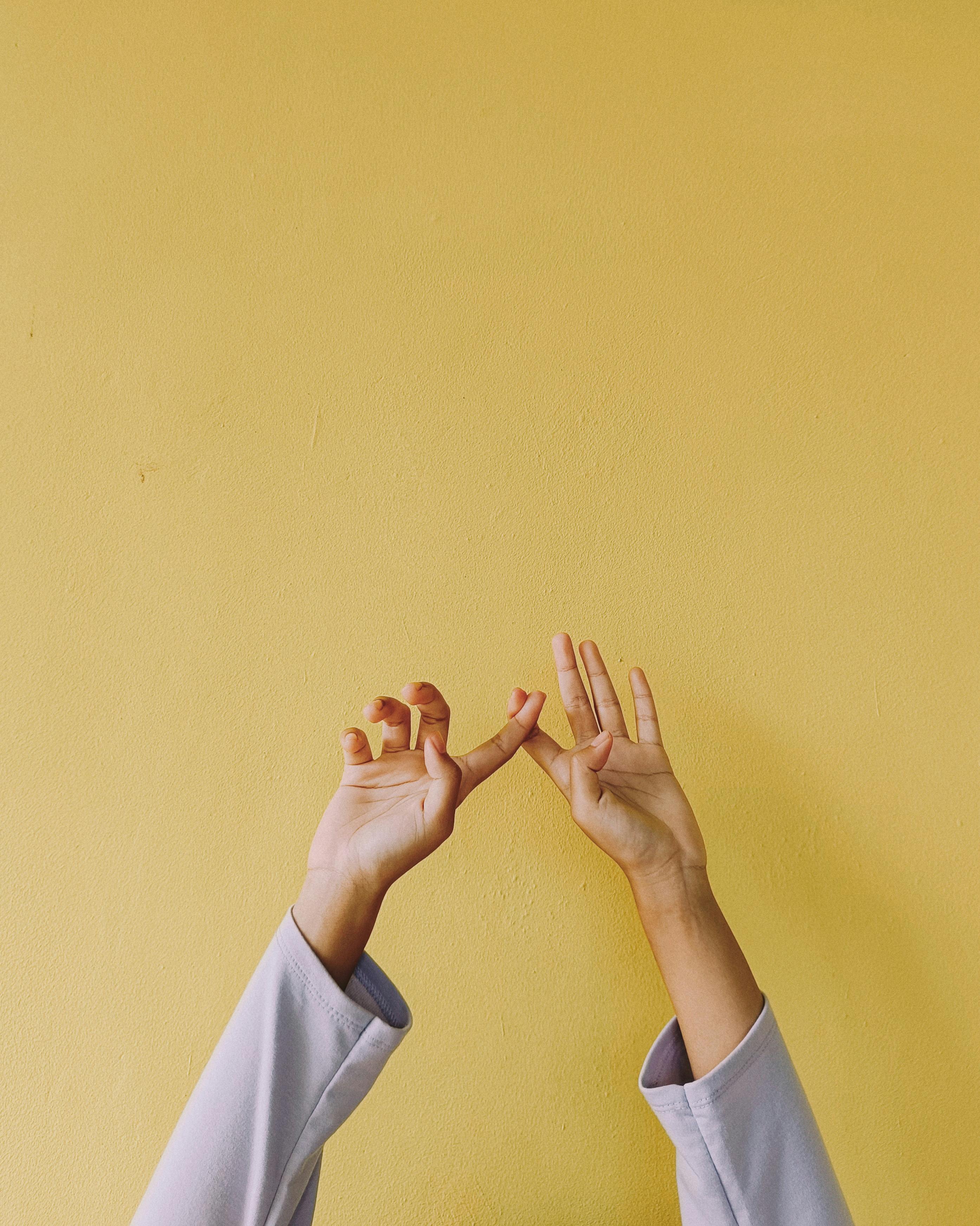 Gratuit Două mâini se ating grațios de un perete galben strălucitor, creând o compoziție minimalistă și artistică. Fotografie de stoc