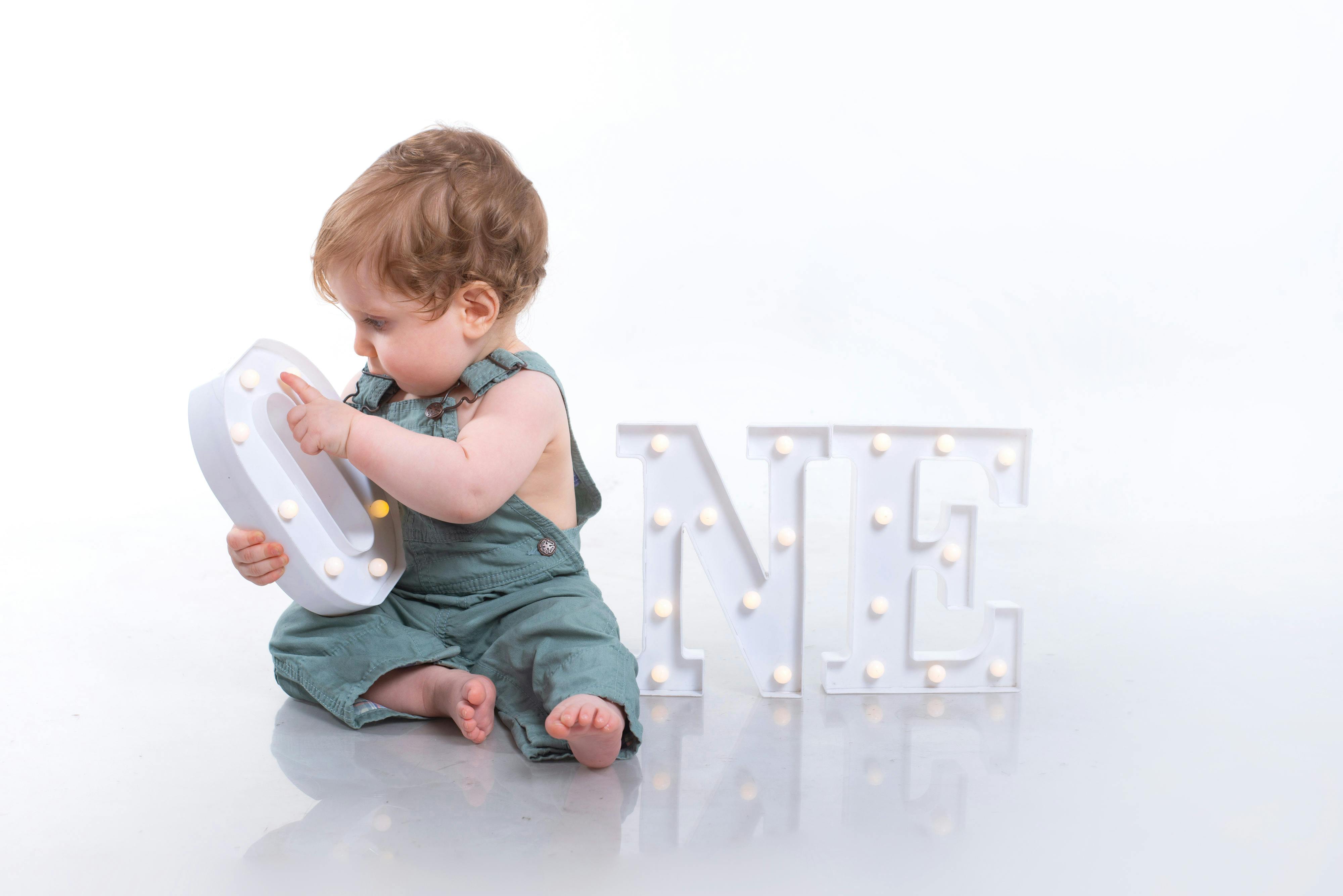 Cute baby sitting with illuminated 'One' sign, celebrating first birthday. Perfect for milestone moments.