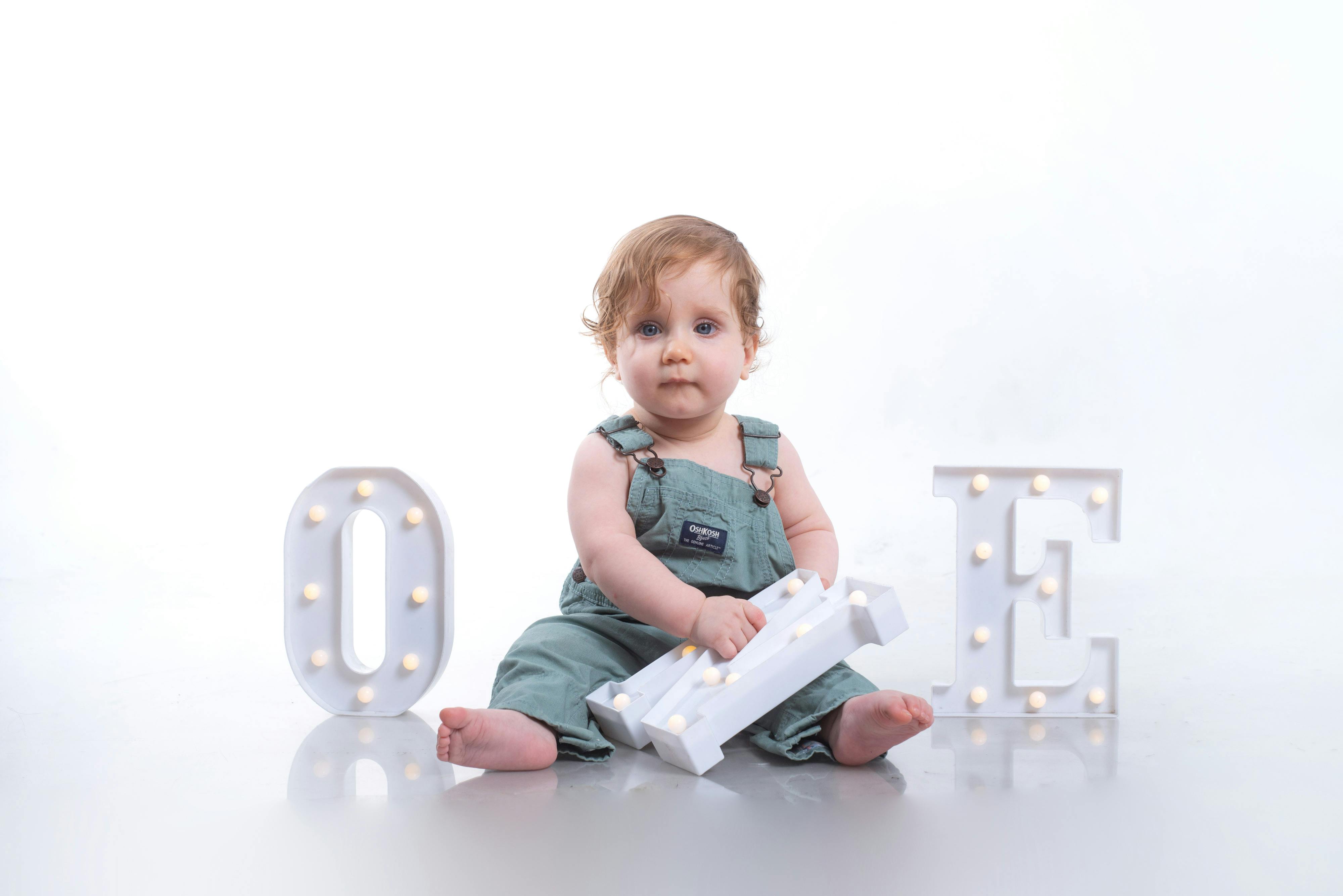 Cute baby sitting with decorative letters 'O', 'N', 'E' for first birthday photo.
