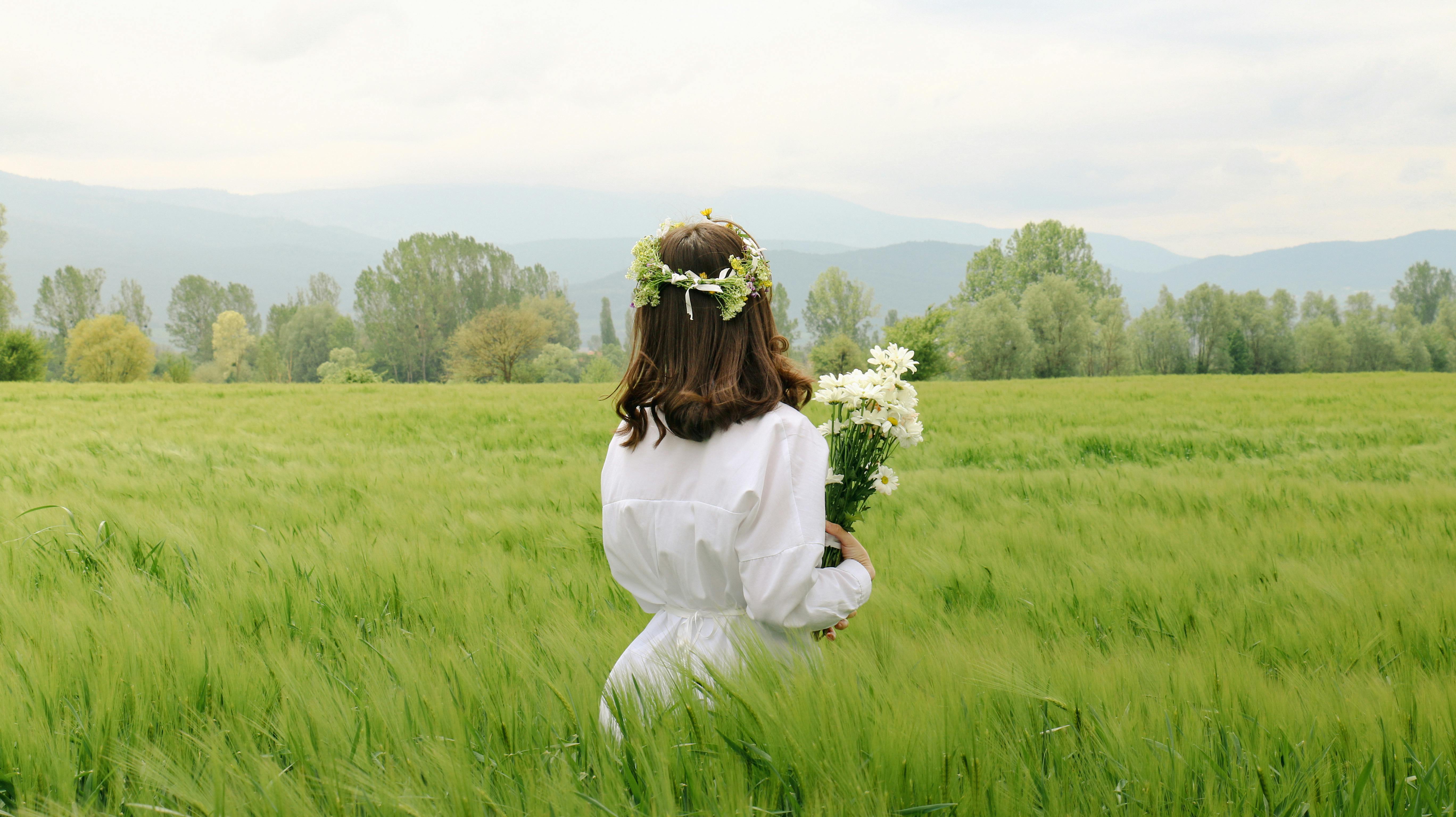 Back view of a woman in a field holding flowers, embracing nature in spring.