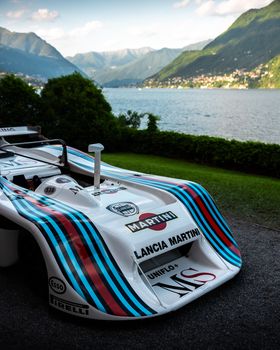 Classic Lancia Martini race car parked by scenic Lake Como with mountains.
