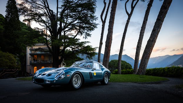 Vintage sports car parked in a stunning lakeside setting, surrounded by tall pine trees during a twilight backdrop.