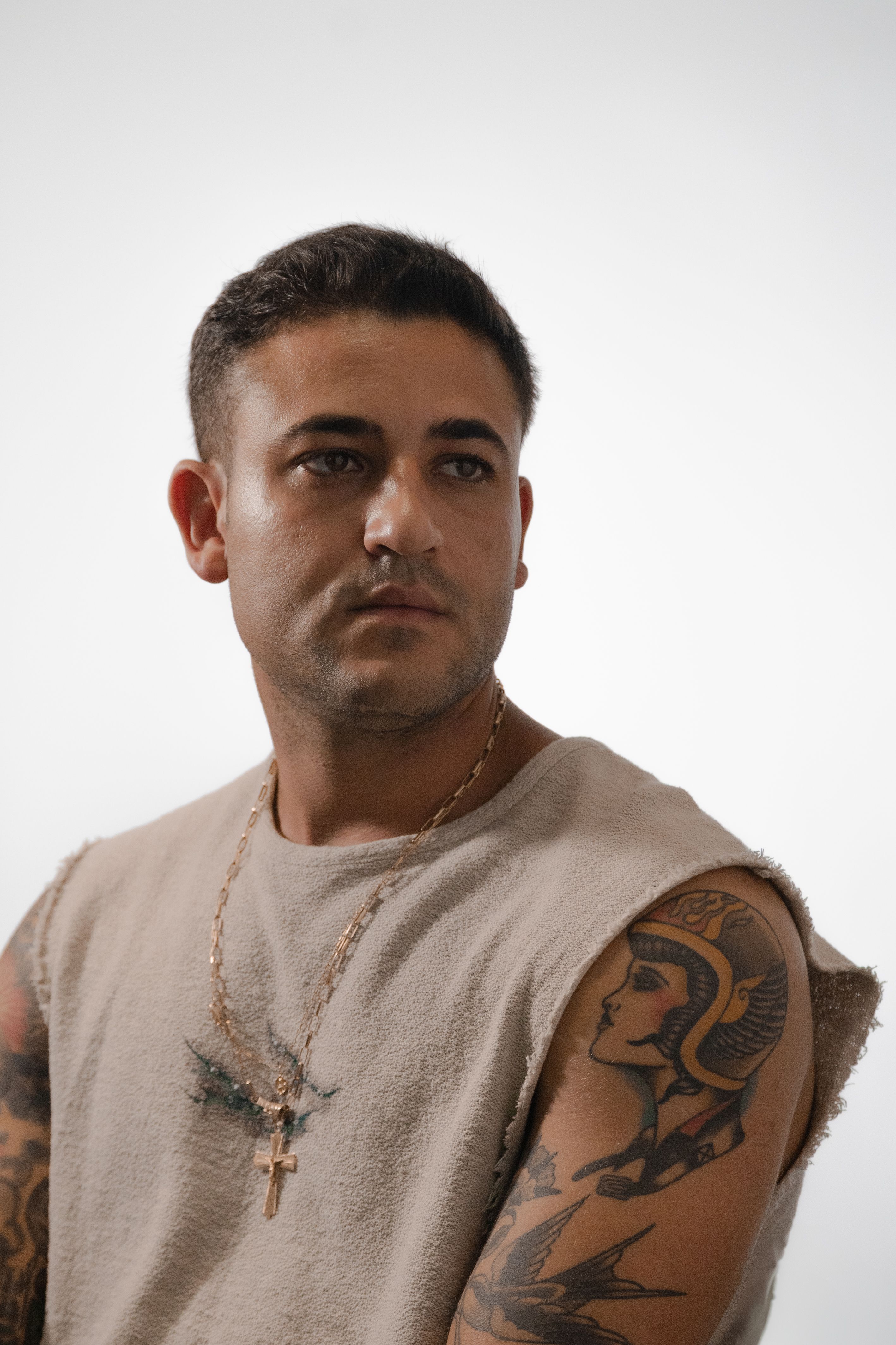 Man with tattoos and necklace against a neutral background portrays modern style and confidence.