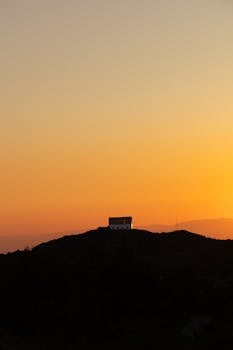 A silhouette of a house on a hill against a glowing orange sunset sky, evoking tranquility.
