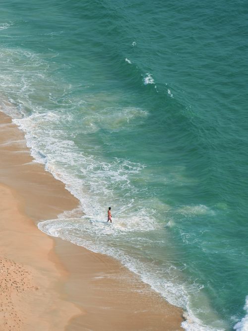Free A person strolls along a tranquil beach with gentle waves lapping at the shore, viewed from above. Stock Photo