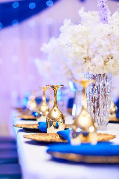 Free Luxurious wedding table setup featuring gold goblets and white floral centerpiece under soft lighting. Stock Photo