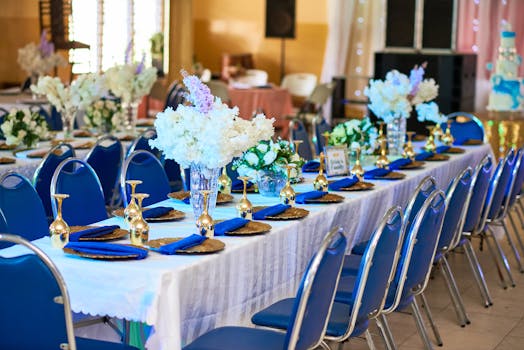 Chic wedding reception setup featuring blue chairs, floral arrangements, and gold accents.