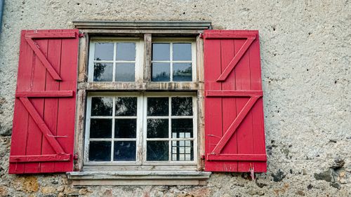 Free A charming window with red shutters on a rustic stone wall, creating a vintage ambiance. Stock Photo