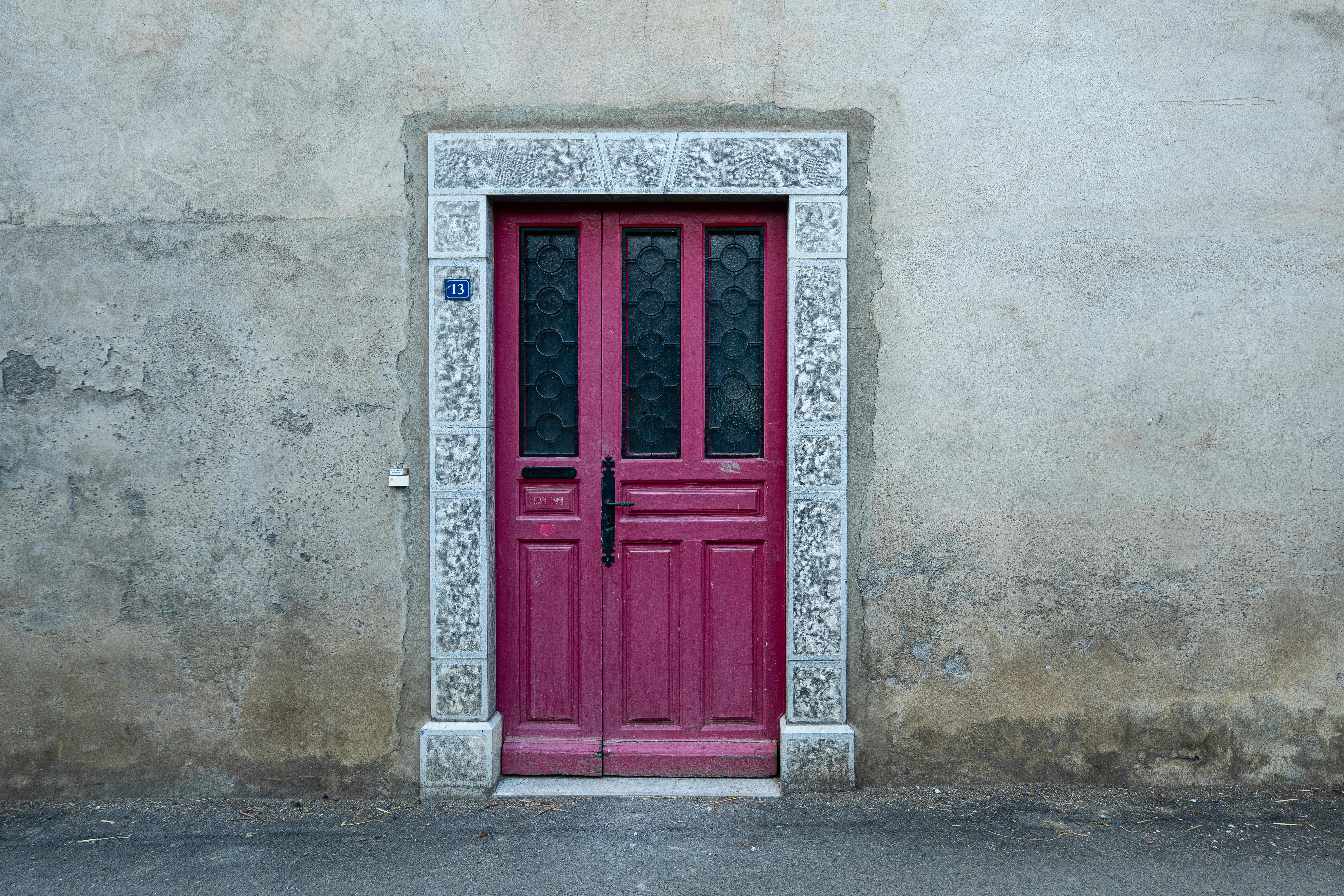Red wooden door with stone frame on a weathered stone wall, number 13 visible.