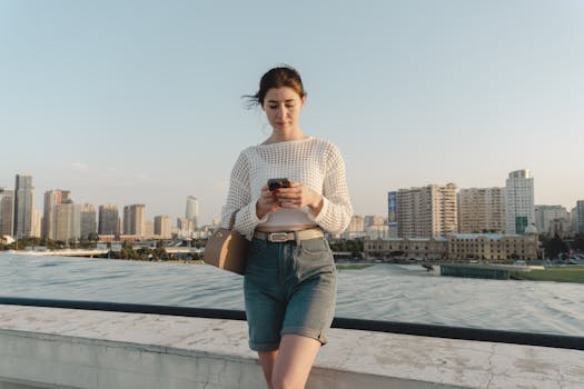 Woman standing on rooftop using smartphone with city skyline in the background.