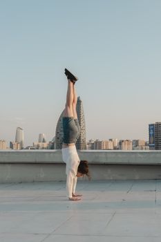 A woman performing a handstand on a rooftop with a city skyline in the background.