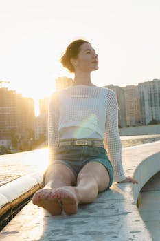 Young woman relaxing on a ledge in the city during sunset, embracing leisure and calm.