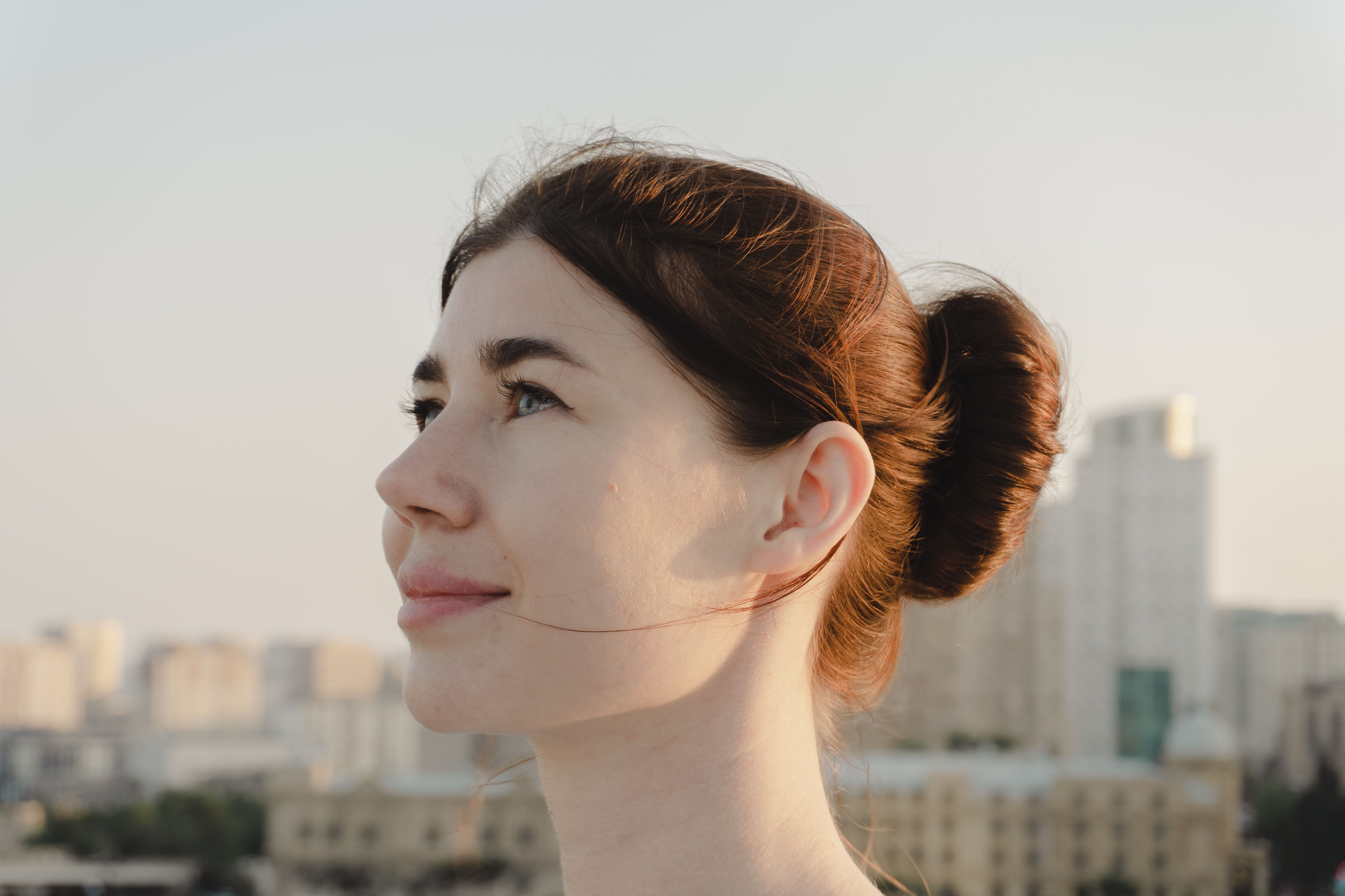 Portrait of a young woman looking hopeful against a city skyline at sunset.