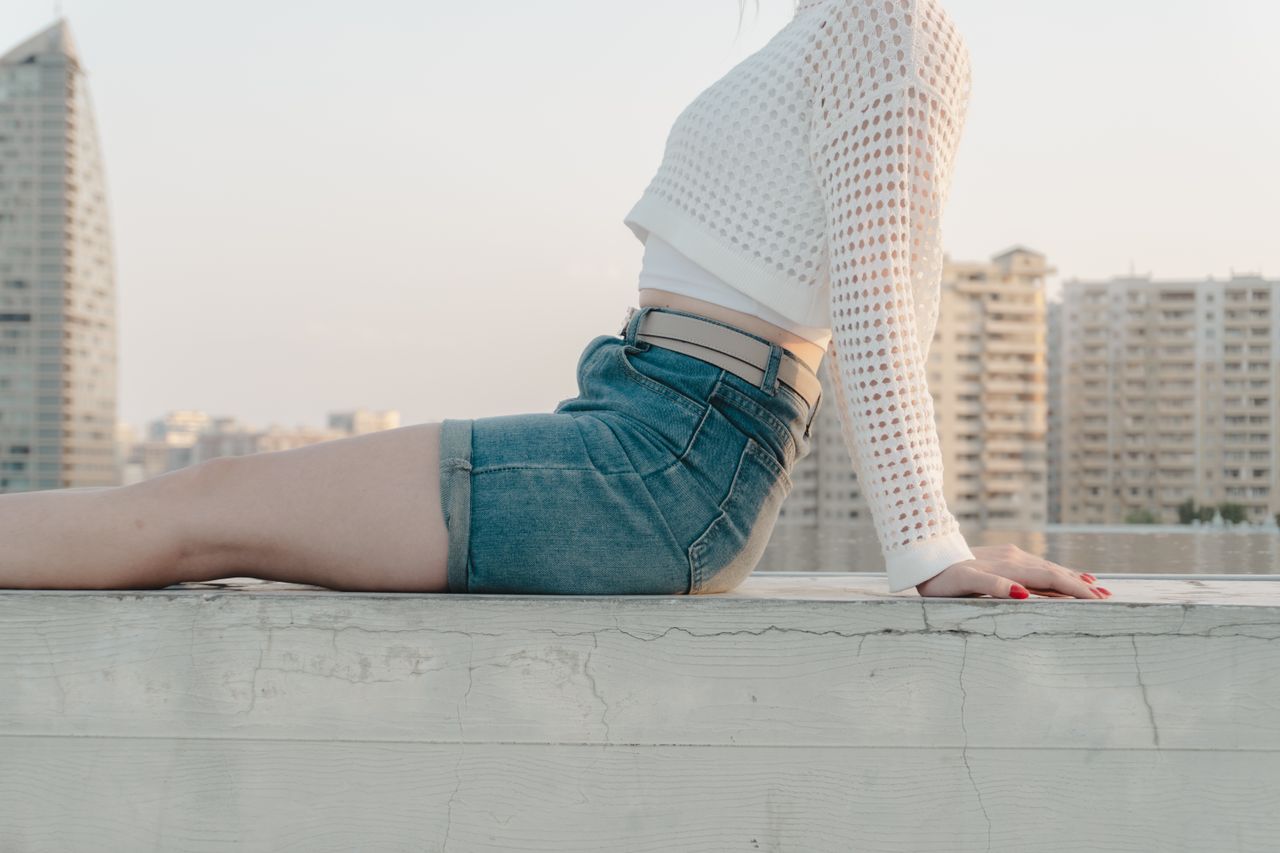 young woman in stylish denim and white top relaxing on city rooftop at