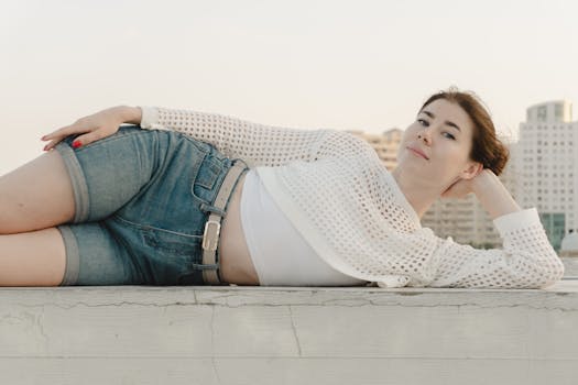 Casual portrait of a young woman lounging on a rooftop with city buildings in the background.