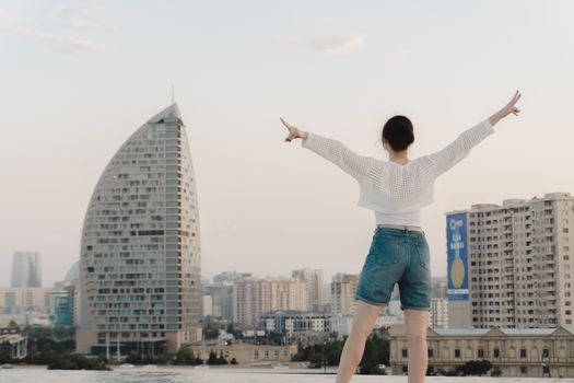 A young woman stands on a rooftop, arms raised, overlooking a modern cityscape during sunset.