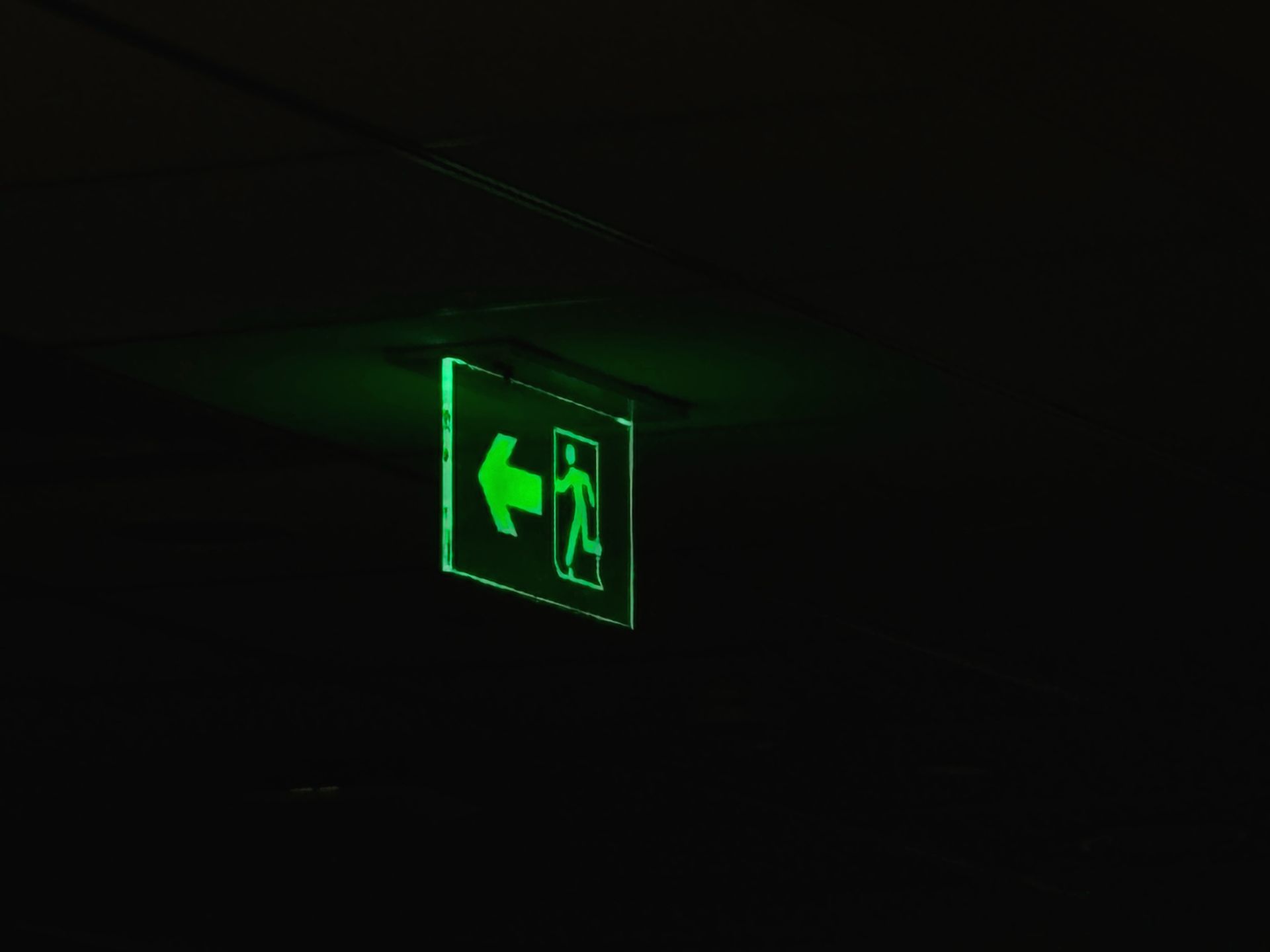 An illuminated green emergency exit sign with directional arrow in a dark setting.
