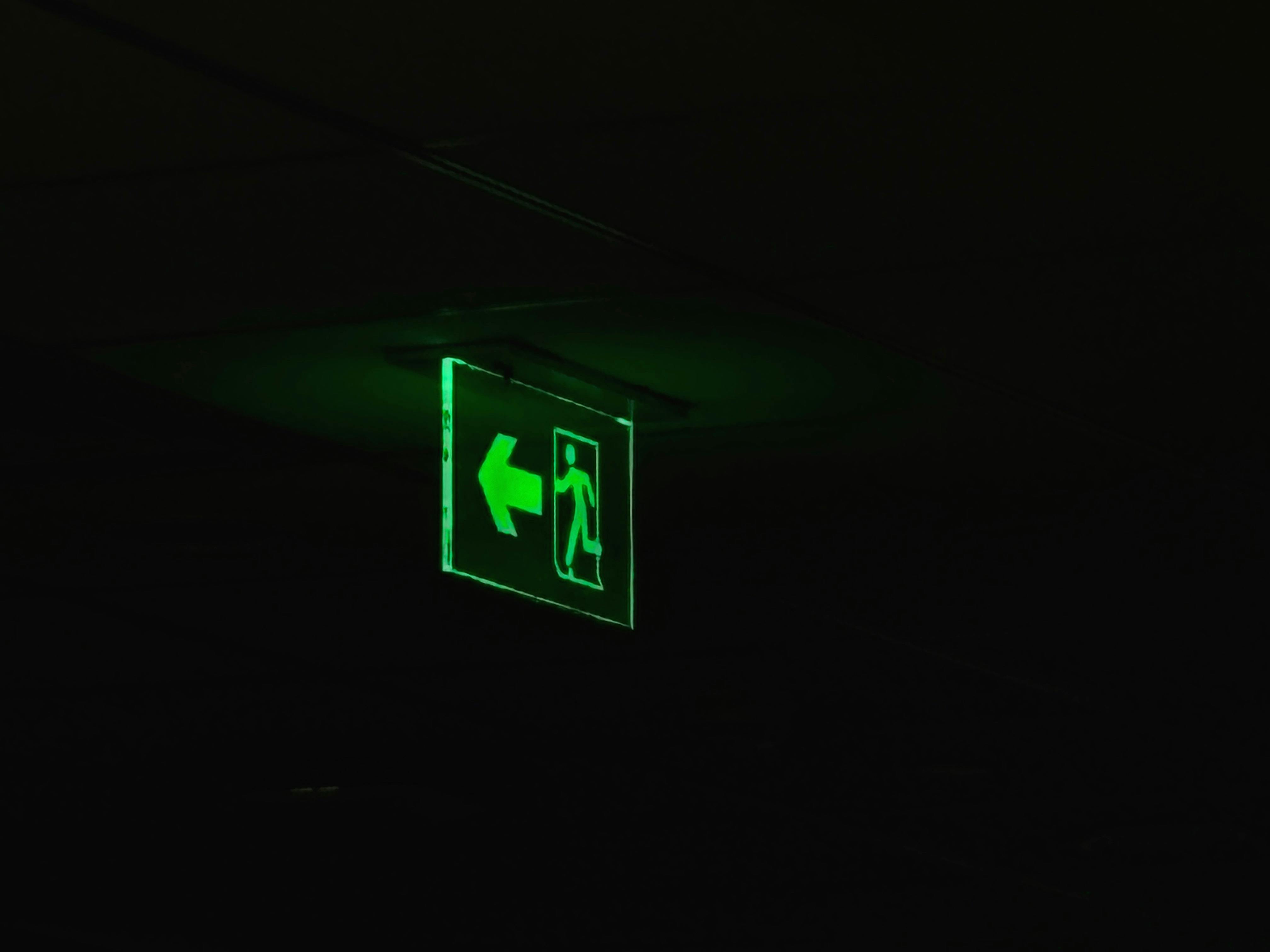 Gratis Una señal de salida de emergencia iluminada en verde con una flecha direccional en un entorno oscuro. Foto de stock
