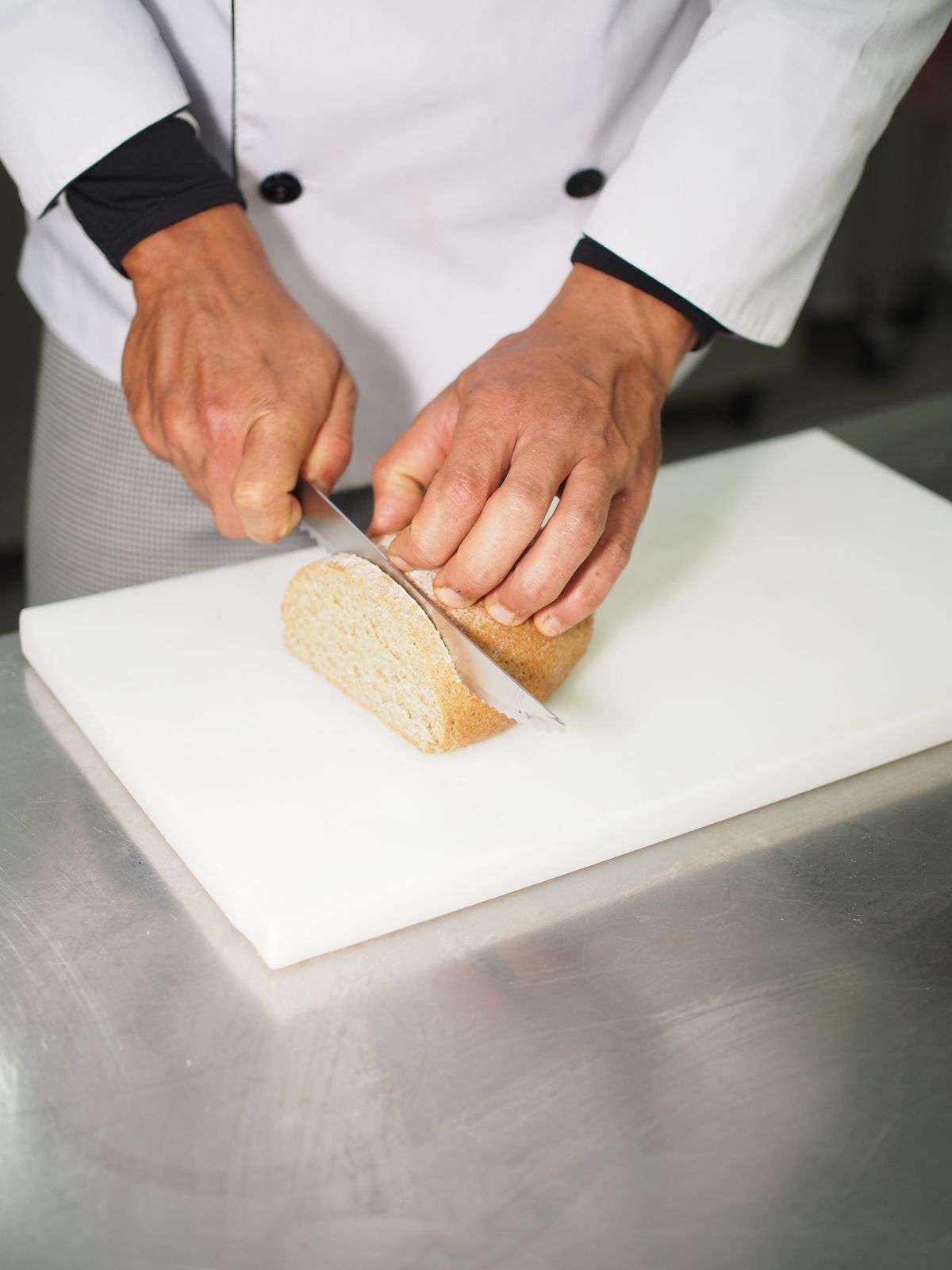 A slicing knife handles bread and bakery items as well as meat Chef slicing fresh bread on a cutting board with a long slicing knife