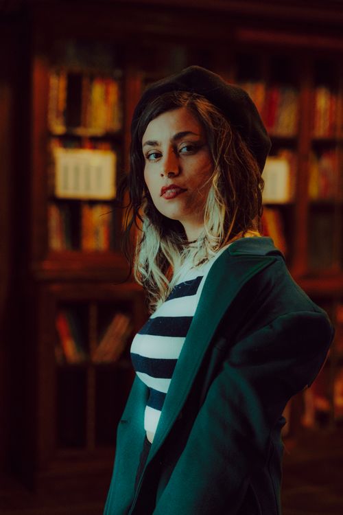 Free Chic woman in a library, wearing a beret and striped top, exuding French style. Stock Photo