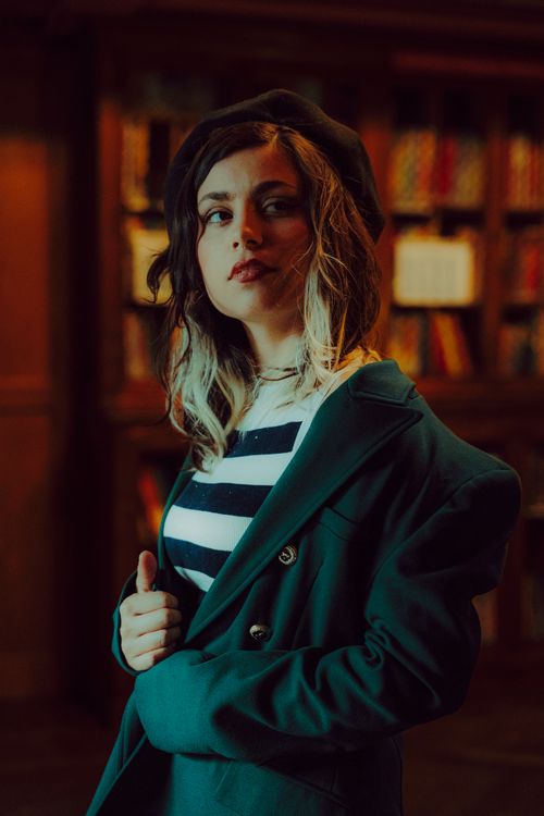 Free Portrait of a fashionable woman in a beret and striped shirt posing elegantly in a library. Stock Photo