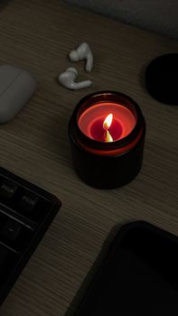A warm, inviting workspace featuring a lit candle and wireless earbuds on a wooden desk.