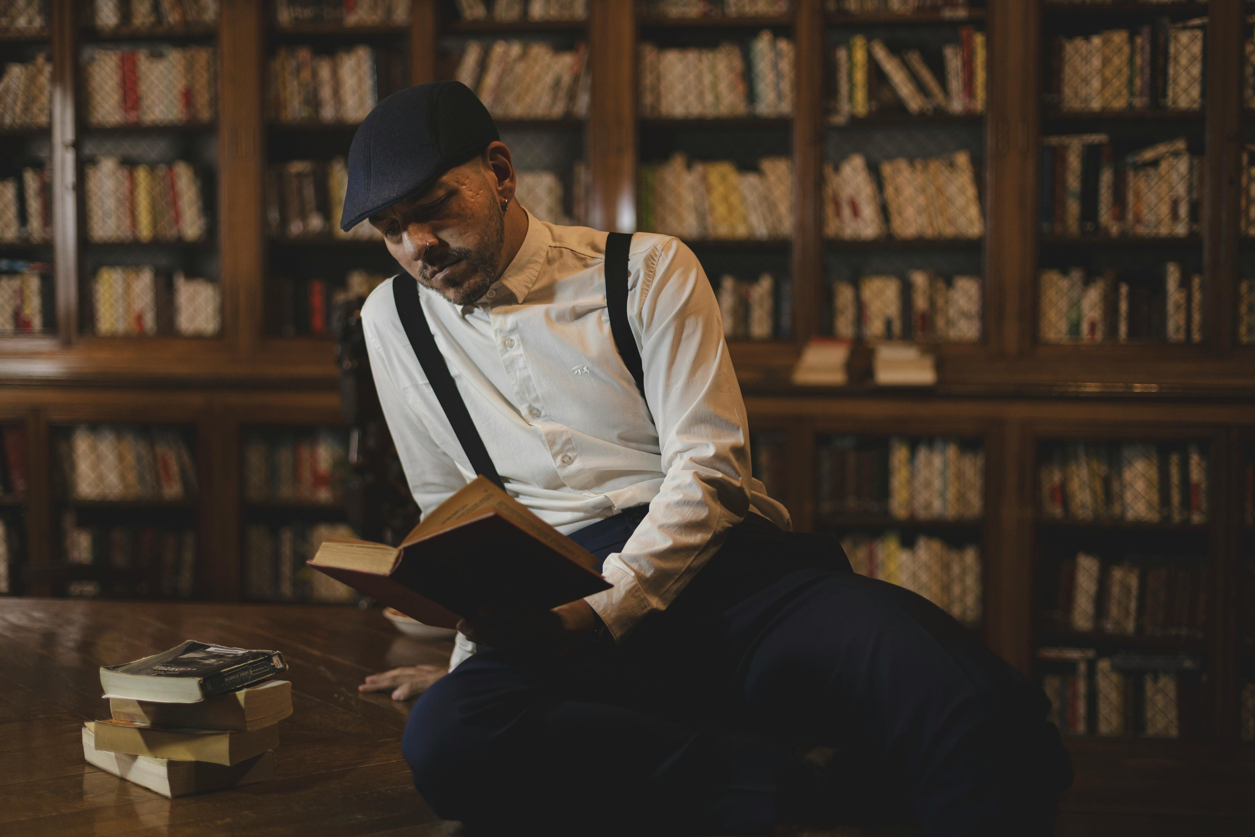 Man sitting in a vintage library, reading a book with focused expression.