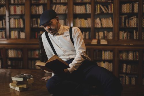 Free Man sitting in a vintage library, reading a book with focused expression. Stock Photo