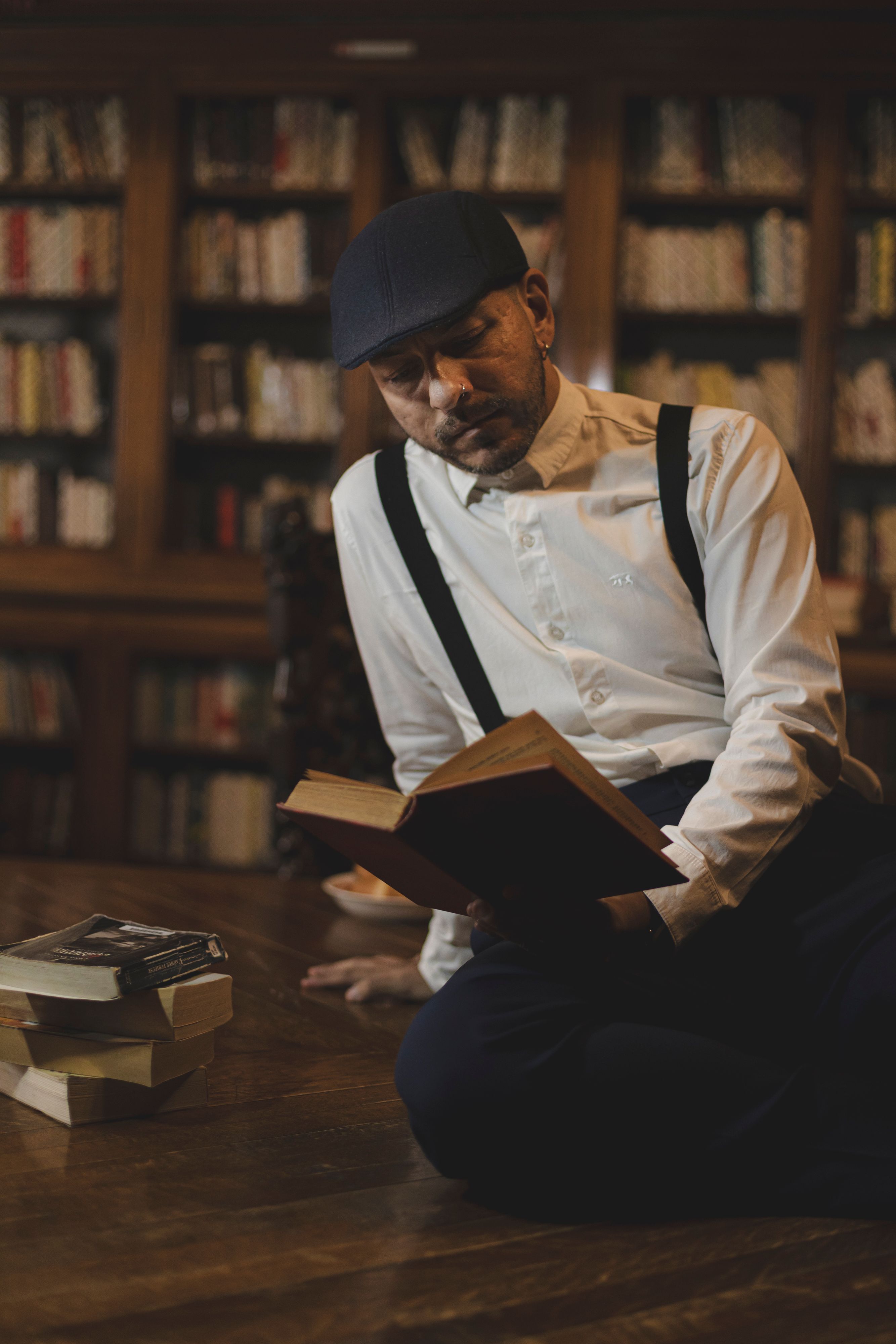 Man in classic attire reading in a warm, cozy library setting in Buenos Aires, Argentina.