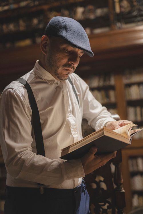 Free A man immersed in reading a book in a classic library with warm ambient lighting. Stock Photo